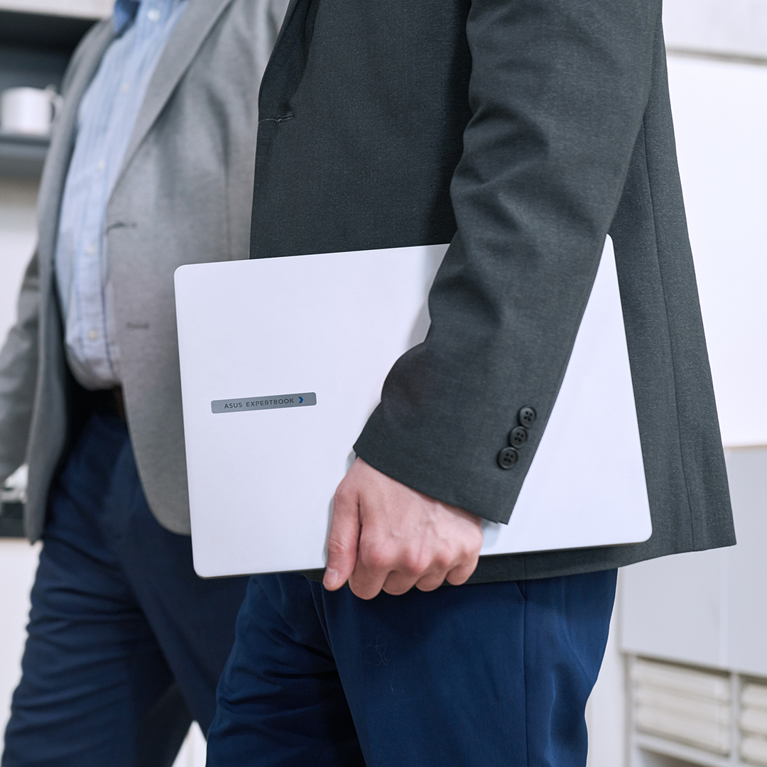 图片聚焦于正在走路的两位男士的腰部，其中一位手上拿着一部 ASUS ExpertBook P 系列。